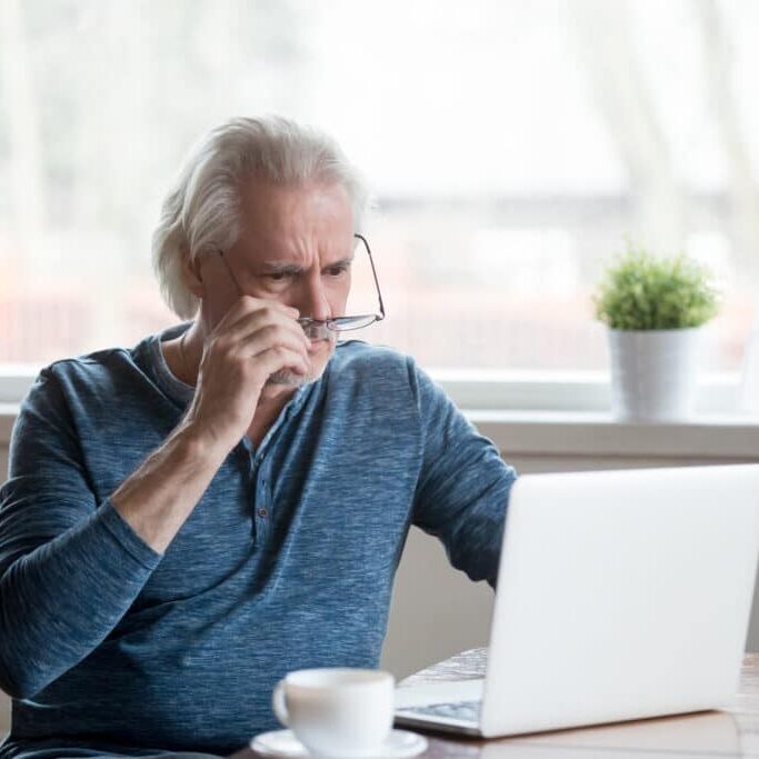 Shocked frustrated senior mature man taking off glasses to look at laptop reading shocking online news at home, stressed worried middle aged old male confused by bad email news or computer problem