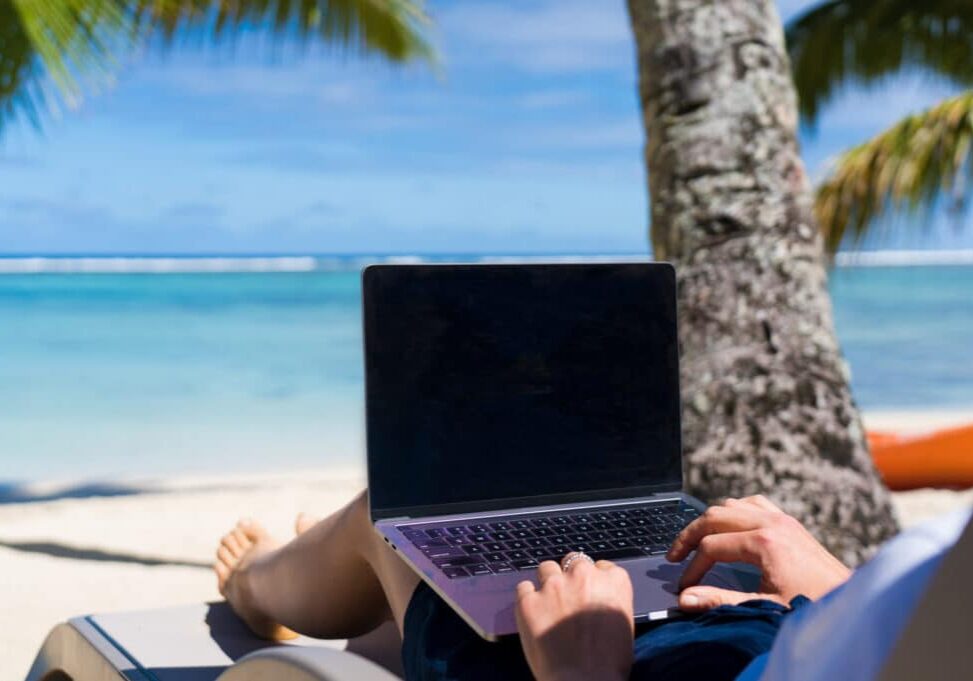 Happy traveler woman enjoys at the tropical beach while working on laptop, Cook Islands, Rarotonga. Summer on beach concept.