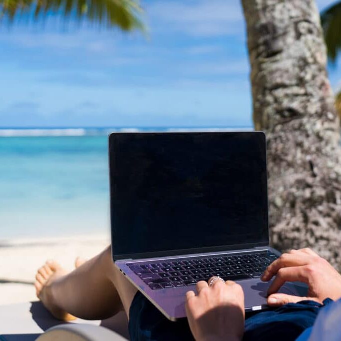 Happy traveler woman enjoys at the tropical beach while working on laptop, Cook Islands, Rarotonga. Summer on beach concept.
