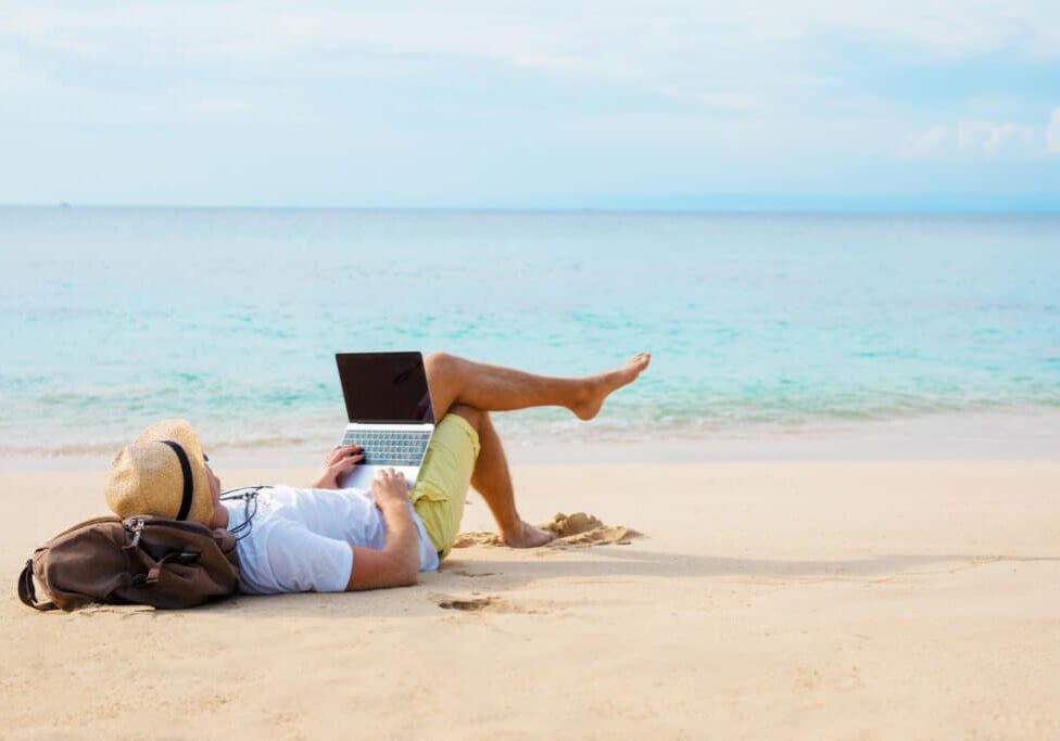 Man working on laptop computer while relaxing on the beach Man working on laptop computer while relaxing on the beach. Idyllic photography covering working anywhere concept.